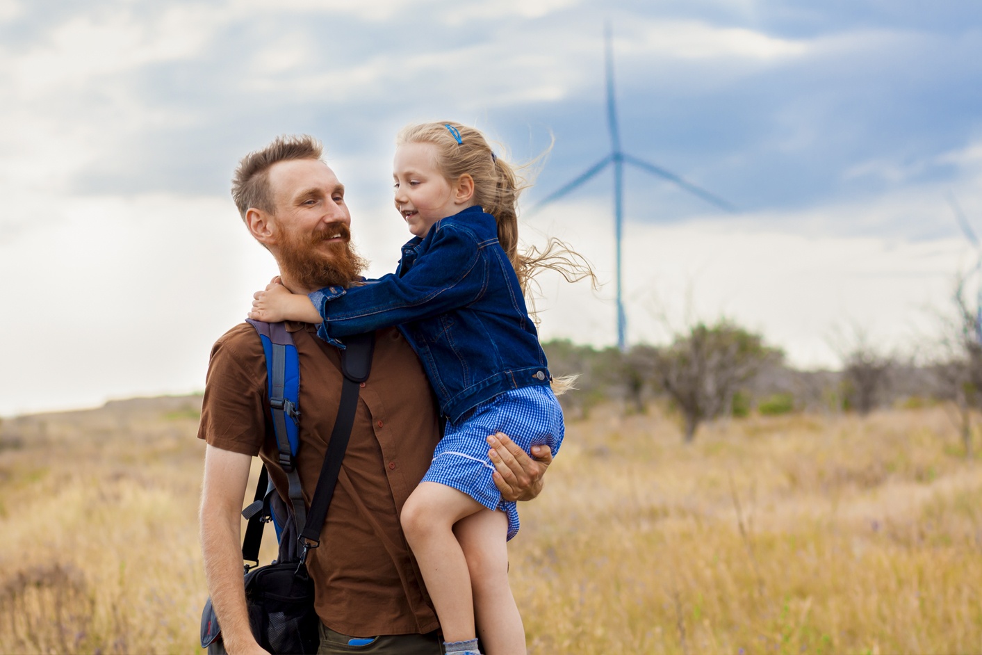 Man holding girl infront of wind turbine